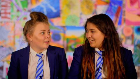 Two girls in school uniform talking and laughing.