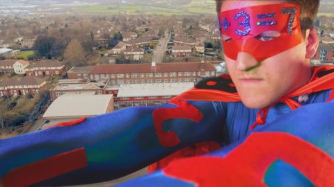 A man dressed as a super hero with a sum on his head flying over a school.