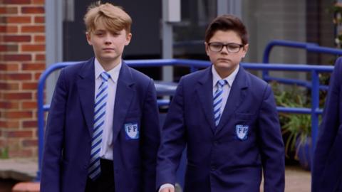 Two boys in school uniform walking and looking very serious.