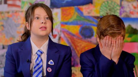 A young girl looking shocked and a boy with his head in his hands.