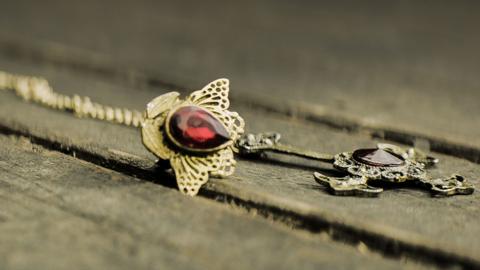 A gold necklace with a big ruby on a wooden floor.