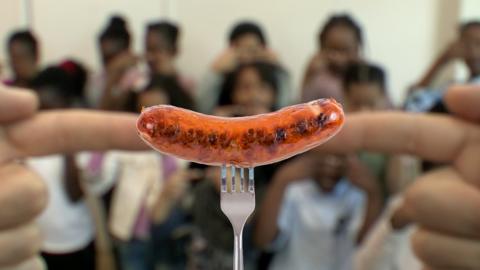 Two blurred fingers coming together, with a sausage on a fork between them.