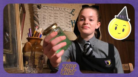 A girl sat at her desk and holding a jar of slime. Ethel from The Worst Witch.