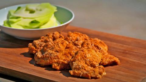 A picture of some chicken resting on a board next to a bowl of salad.