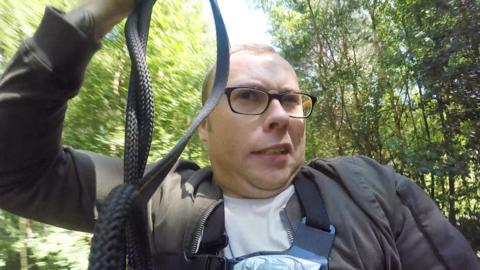 A close-up picture of the presenter, Joe, on a zip wire looking scared.