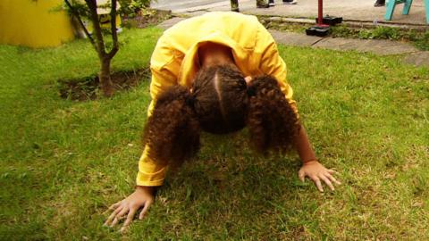 A young girl in a yellow boiler suit doing a push up.