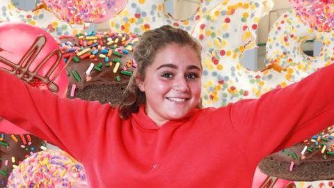 Matilda Ramsay in front of multiple doughnuts.