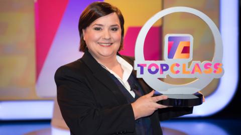 A lady (Susan Calman) holding the Top Class trophy.