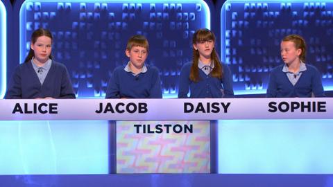 Four pupils sit behind a studio gameshow desk.