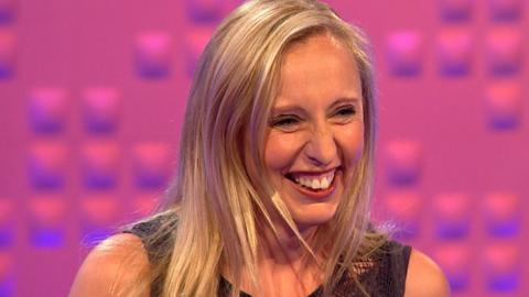 A woman laughs against a pink background.