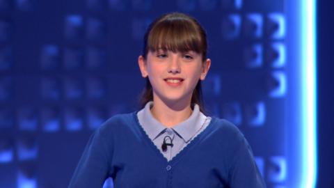 A girl wearing a blue school uniform smiles.