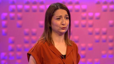 A woman with an orange top looks unsure.