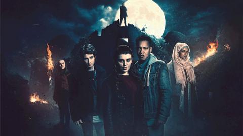 Jana, TJ, Selina, Matai and Amelia stand in a dark wood with a man stood on top of a castle ruin behind them under a full moon.