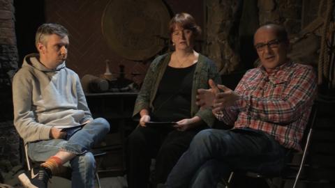 A woman and two men sat in a low lit room next to each other.