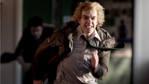 A boy runs down a corridor with a man chasing him.