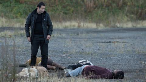 Man looks menacingly over four people lying on the ground.