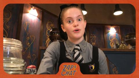 A girl in school uniform at her desk. Ethel from The Worst Witch.