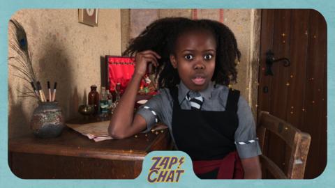 A girl at her desk looks shocked. Beatrice from The Worst Witch.