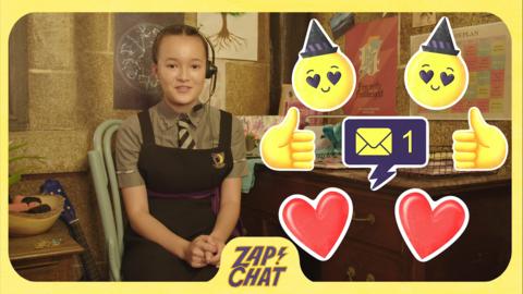 A young witch wearing a headset smiles, with an emoji heart and smilies next to her.