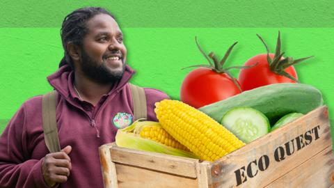 Ranger Hamza is smiling next to a wooden crate of different vegetables