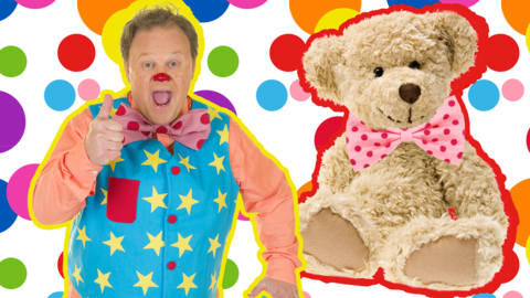 Mr Tumble is smiling with his thumb up to camera, Tumble Ted is sat next to him - they are both in front of a spotty background.