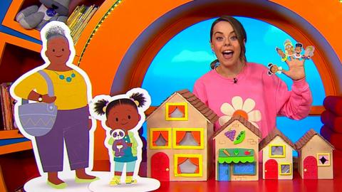 CBeebies House where Evie is holding up JoJo & Gran Gran finger puppets.