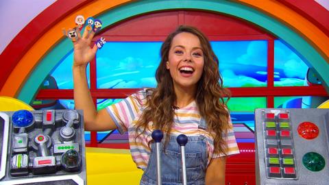 Evie from CBeebies House is smiling to camera with her right arm in the air. On her hand is a character from Go Jetters on each of her fingers and thumb.