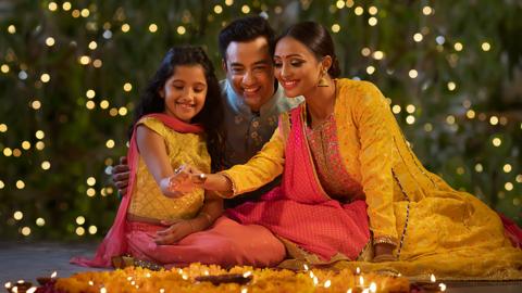 A mother, father and child are sitting on the floor celebrating Diwali.