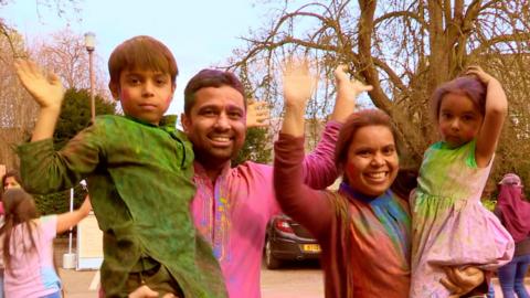 A family of four are smiling and waving.