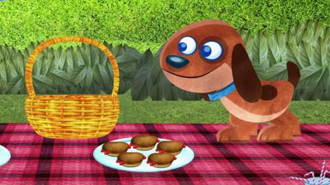 A dog stood on a picnic blanket next to a picnic basket. In front of him is a plate with five buns on it.