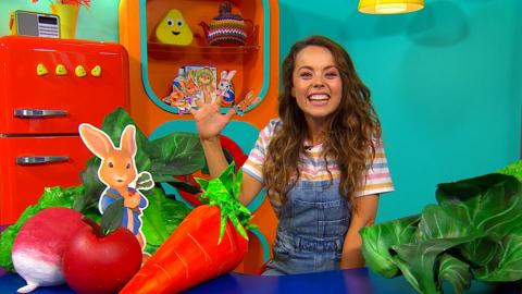 Evie from CBeebies House is smiling to camera with her hand up and Peter Rabbit characters on each finger and thumb