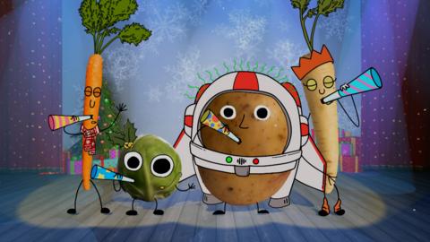 A carrot, parsnip, potato and brussel sprout are on a stage, wearing party hats and blowing party whistles.