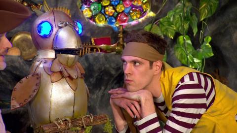 SEaweed is leaning on his hands whilst looking at a metal parrot with blue eyes that are lit up.