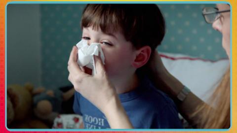 Child blowing his nose with help from his mum.