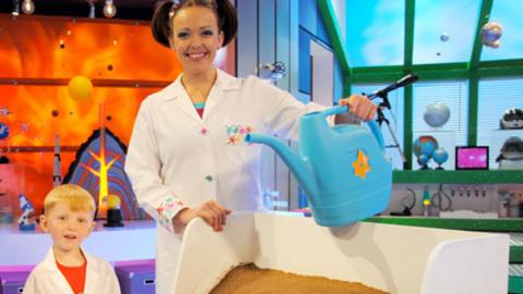 Two Earth Explorers and Nina in her lab, holding a watering can