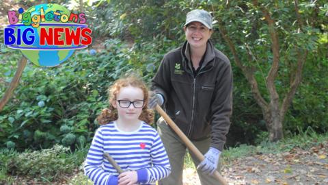 Mimi is in a garden with Fiona holding gardening rakes.