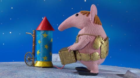 Major Clanger from The Clangers holding a box next to a rocket.