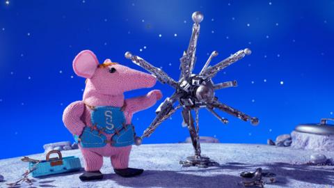 Small Clanger from The Clangers next to a metallic star-shaped object.