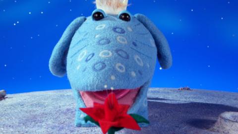 A Skymoo from The Clangers standing open-mouthed in front of a blooming Star Rose.