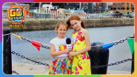 Go Jetters Radio Recruits Ayesha and Brooke are standing next to the docks with boats in the background.