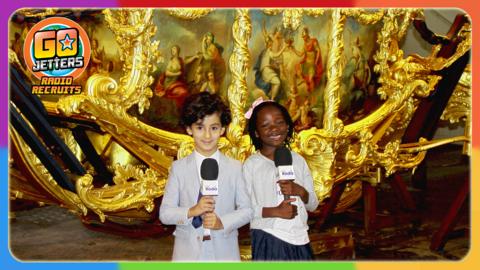 Go Jetters Radio Recruits Abdul and Kezia are in Buckingham Palace holding CBeebies Radio microphones and standing in front of a golden carriage.