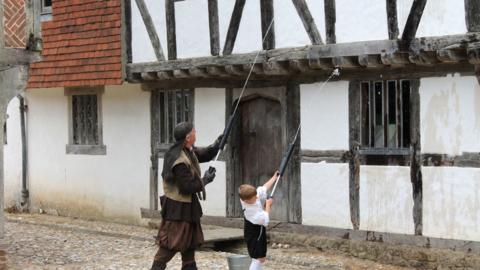 Two people dressed in Elizabethan costume pouring water on a timber-frame house.