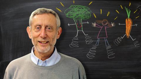 Michael Rosen from Poetry Playtime in front of a blackboard picture of vegetables and people with springs on their feet.