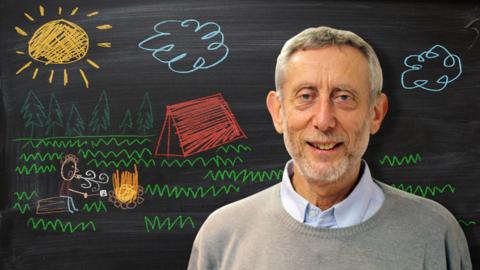 Michael Rosen from Poetry Playtime in front of a blackboard picture of a man blowing on a campfire.