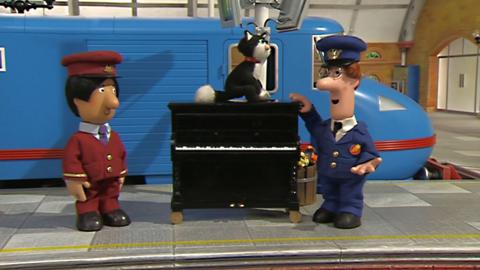 Pat, Jess and Ajay from Postman Pat: Special Delivery Service with a piano by a train in a station.