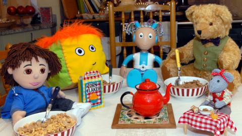 Tom, Stuffy, Mo Mo, Teddington and Miss Mouse from Show Me Show Me sitting around a table eating breakfast.