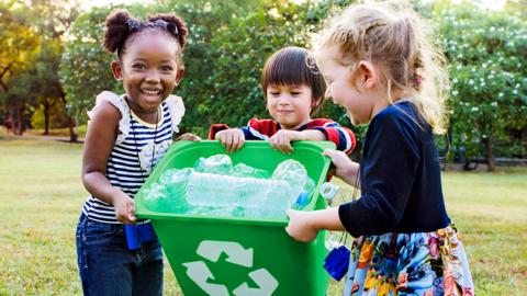 Tips to get kids recycling, children hold green recycling tub with plastic bottles in it.