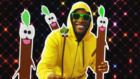 Presenter dressed in a yellow hoodie and sunglasses with his stick friend and sticks surrounding him