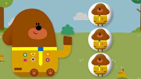 Duggee is sitting on grass, there are three circle buttons next to him with duggee illustrations on them.