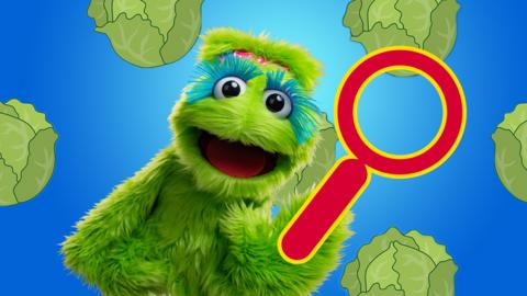 Little Monster, a green fluffy puppet with a red magnifying glass and sprouts in the background.